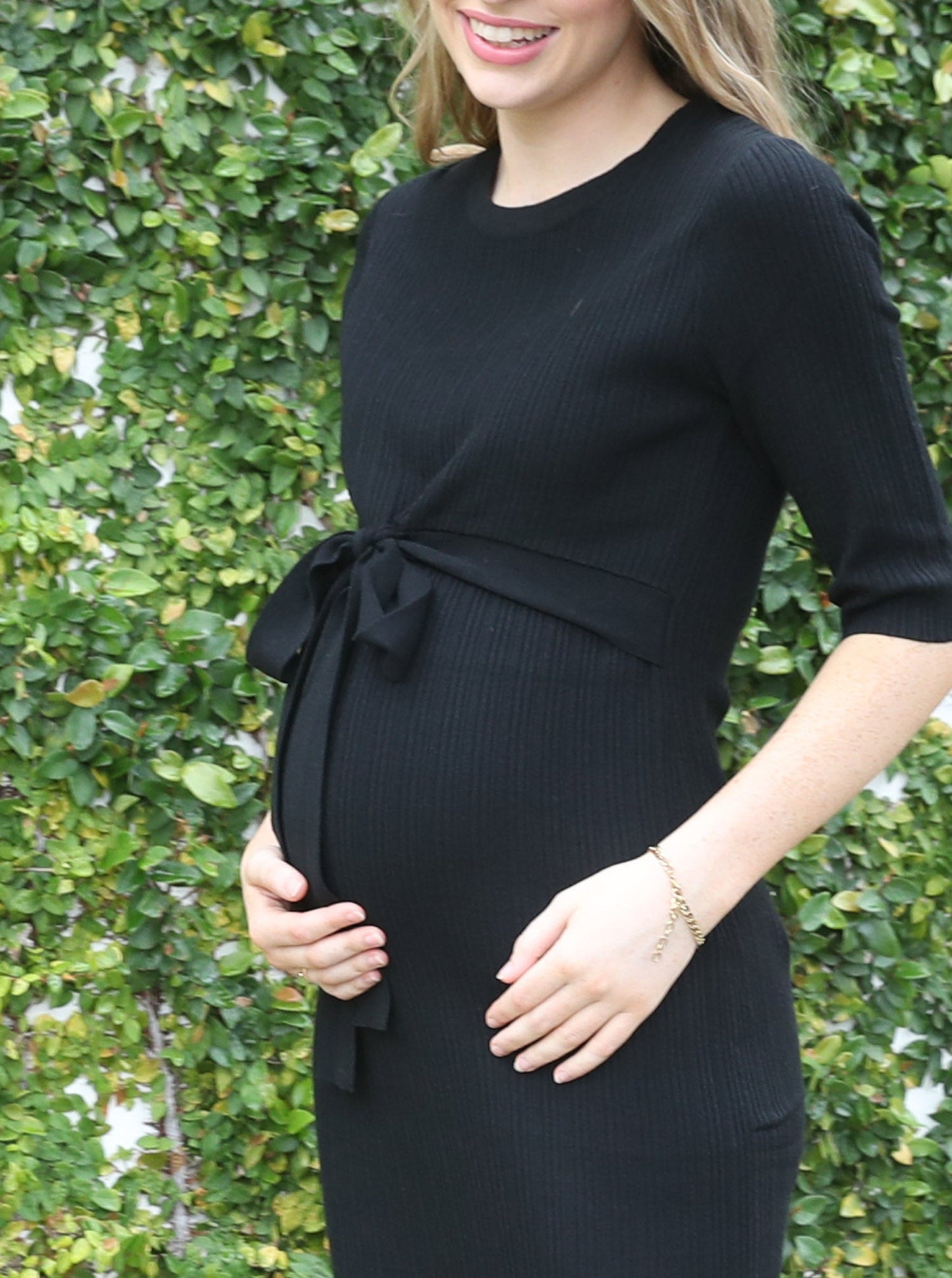 A woman in black angel maternity annabella knit dress against the wall, stretchy (6594399666279)